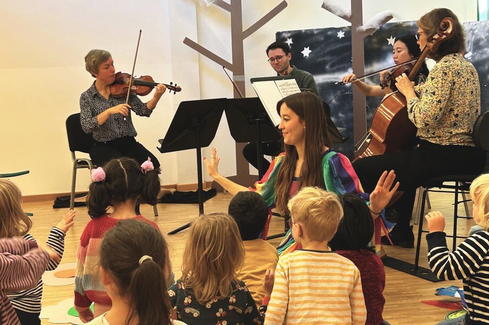 Kinder und Erwachsene sitzen gemeinsam auf dem Boden, singen und musizieren