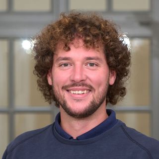 Portraitfoto von Andre Unnewehr, mit braunen Locken und kurzem Bart.