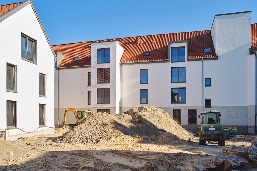 Der Innenhof mit aufgeschüttetem Sand im Sonnenschein. Die neue helle Fassade strahlt in der Sonne.