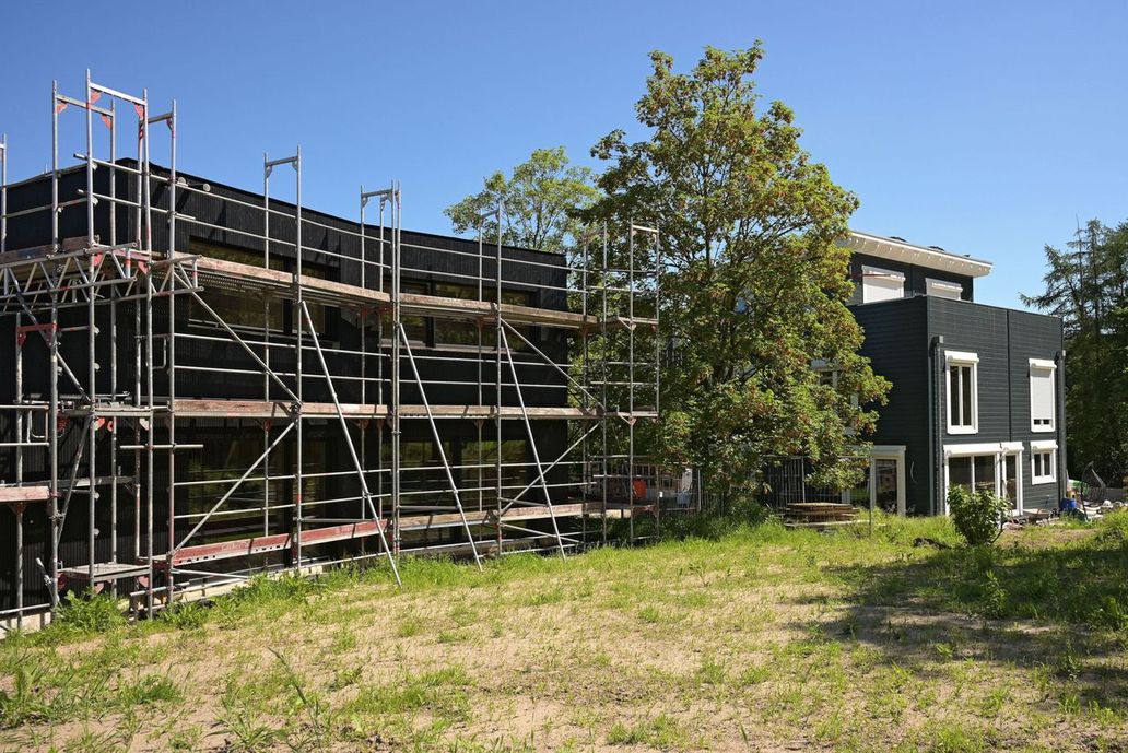 Eingerüstetes Gebäude im Bau, neben dem schwarz-weißen Holzhaus
