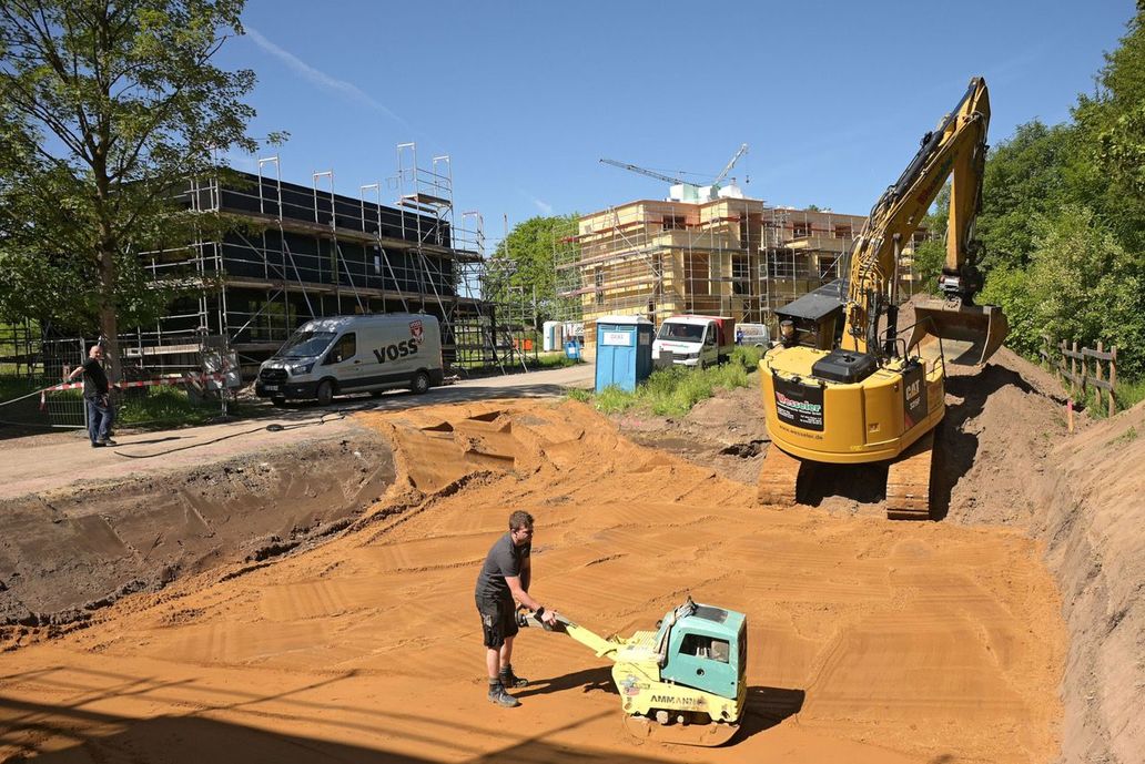 Auf der Baustelle: ein Bauarbeiter mit einem Rüttler festigt den Sandboden