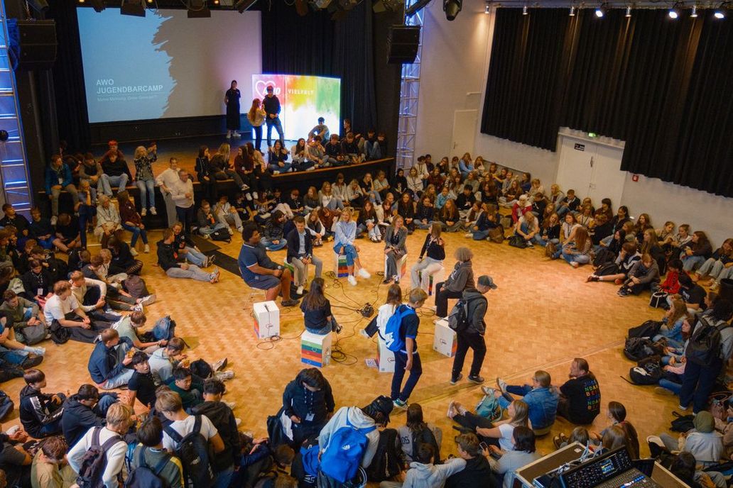 Teilnehmer*innen sitzen auf dem Boden des gut gefüllten Seminarsaals, in der Mitte ist eine Diskussionsrunde aufgebaut
