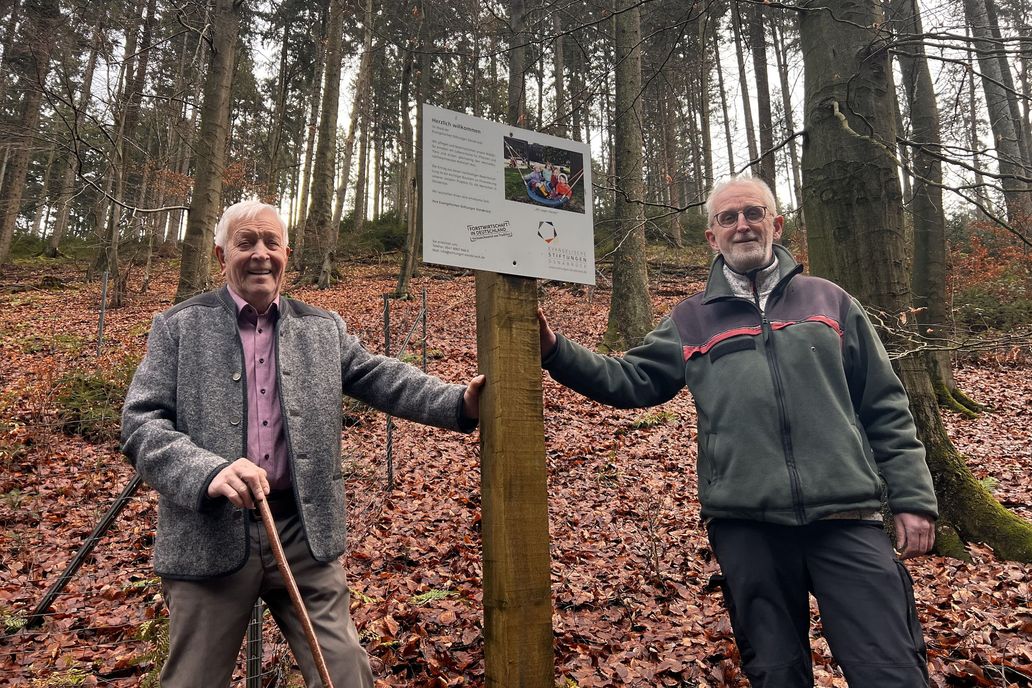 Herbert Schwietert und Friedrich Gleissner im Wald mit dem Hinweisschild der evangelischen Stiftungen Osnabrück